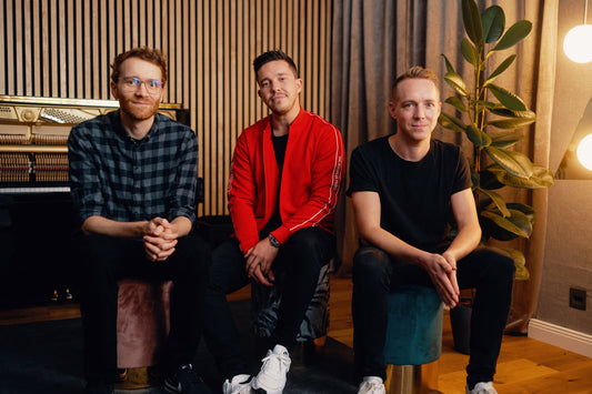 Nico Santos, Kalli Reinhardt & Joe Walter sitting on a bench looking into camera